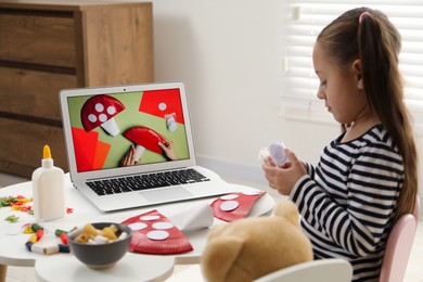 Photo of Little girl making handmade fly agaric by following craft tutorial video at home. Child creativity