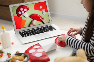 Photo of Little girl making handmade fly agaric by following craft tutorial video at home. Child creativity