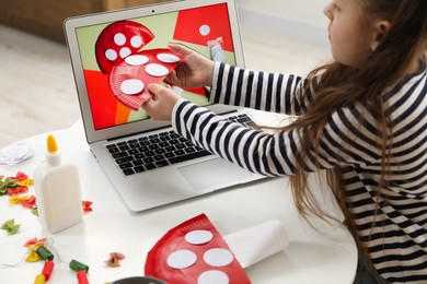 Photo of Little girl making handmade fly agaric by following craft tutorial video at home. Child creativity