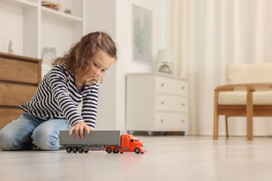 Photo of Little girl playing with toy car on floor at home, space for text