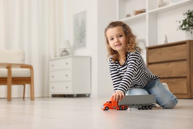 Photo of Little girl playing with toy car on floor at home, space for text