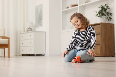 Photo of Little girl playing with toy car on floor at home, space for text