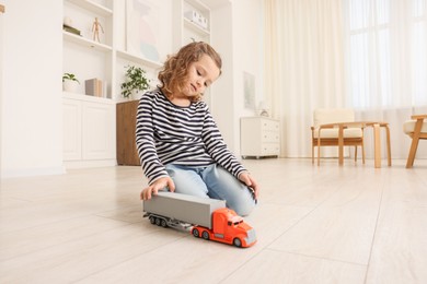 Photo of Little girl playing with toy car on floor at home, space for text