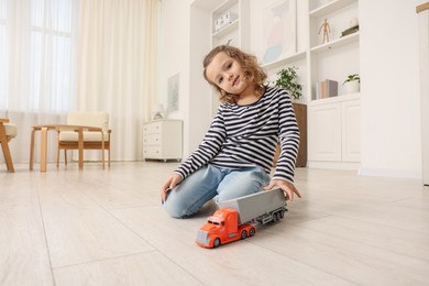 Photo of Little girl playing with toy car on floor at home, space for text