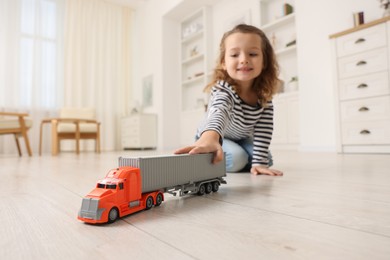 Photo of Little girl playing with toy car on floor at home, selective focus