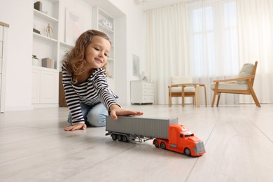 Photo of Little girl playing with toy car on floor at home