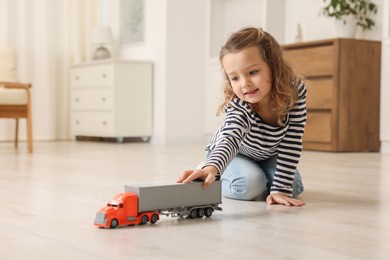 Photo of Little girl playing with toy car on floor at home