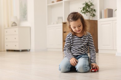 Photo of Little girl playing with toy car on floor at home, space for text