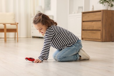 Photo of Little girl playing with toy car on floor at home