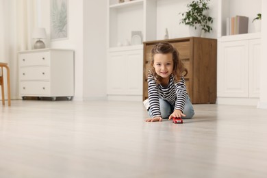 Photo of Little girl playing with toy car on floor at home, space for text