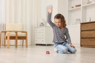 Photo of Little girl playing with toy car on floor at home, space for text