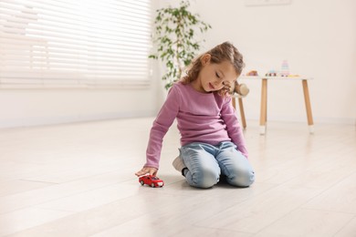 Photo of Little girl playing with toy car on floor at home, space for text