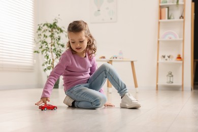 Photo of Little girl playing with toy car on floor at home, space for text