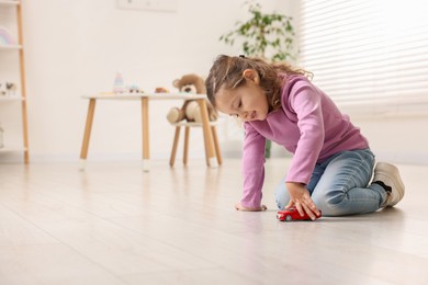 Photo of Little girl playing with toy car on floor at home, space for text