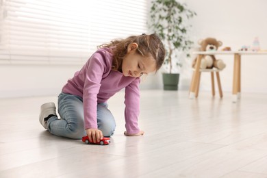 Photo of Little girl playing with toy car on floor at home, space for text