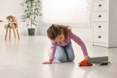 Photo of Little girl playing with toy car on floor at home