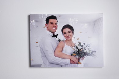 Photo of Canvas with printed photo of happy newlyweds on white wall indoors