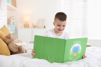 Photo of Bedtime. Cute boy reading book on bed indoors