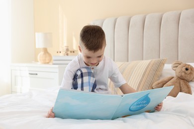 Photo of Bedtime. Cute boy with teddy bear reading book on bed indoors