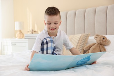 Photo of Bedtime. Cute boy with teddy bear reading book on bed indoors