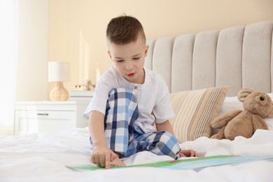 Photo of Bedtime. Cute boy with teddy bear reading book on bed indoors