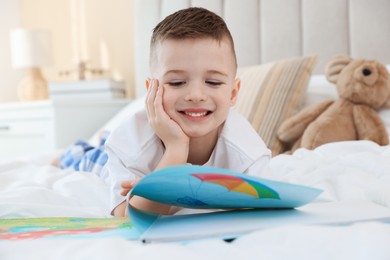 Photo of Bedtime. Cute boy reading book on bed indoors