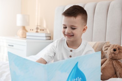 Photo of Bedtime. Cute boy with teddy bear reading book on bed indoors