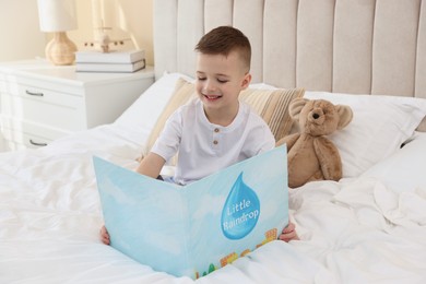 Photo of Bedtime. Cute boy with teddy bear reading book on bed indoors