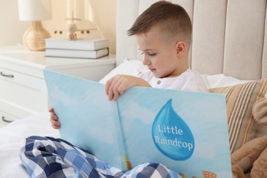 Photo of Bedtime. Cute boy reading book on bed indoors