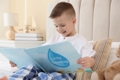 Photo of Bedtime. Cute boy reading book on bed indoors