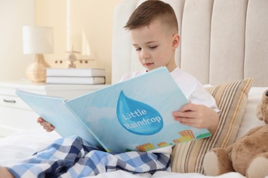 Photo of Bedtime. Cute boy reading book on bed indoors