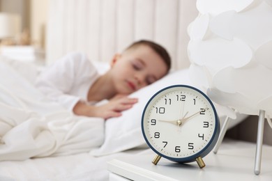 Photo of Bedtime. Cute boy sleeping in bed and alarm clock on bedside table, selective focus