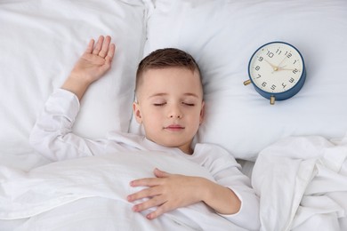 Photo of Bedtime. Cute boy sleeping and alarm clock in bed