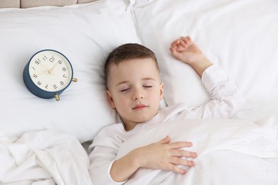 Photo of Bedtime. Cute boy sleeping and alarm clock in bed