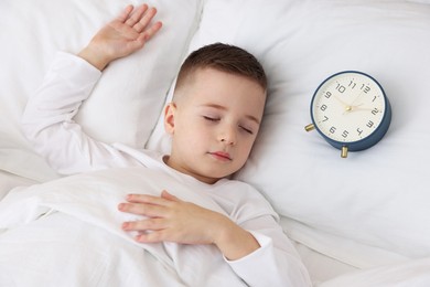 Photo of Bedtime. Cute boy sleeping and alarm clock in bed