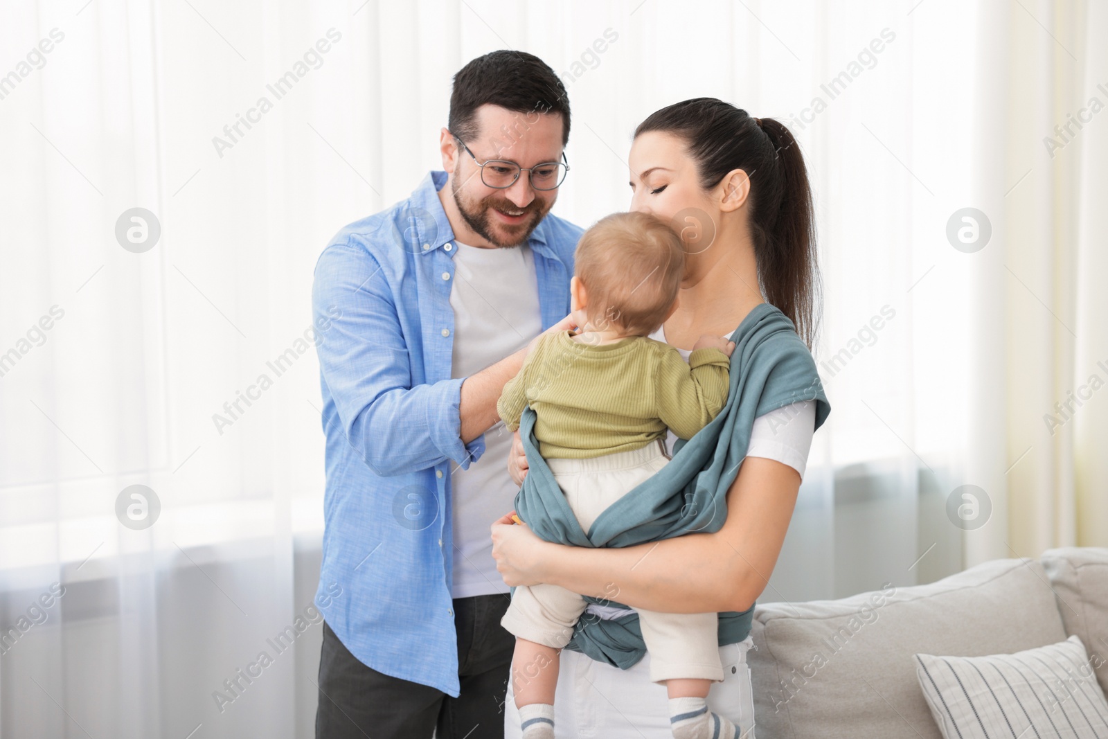 Photo of Portrait of happy family indoors. Mother holding her child in sling (baby carrier) at home