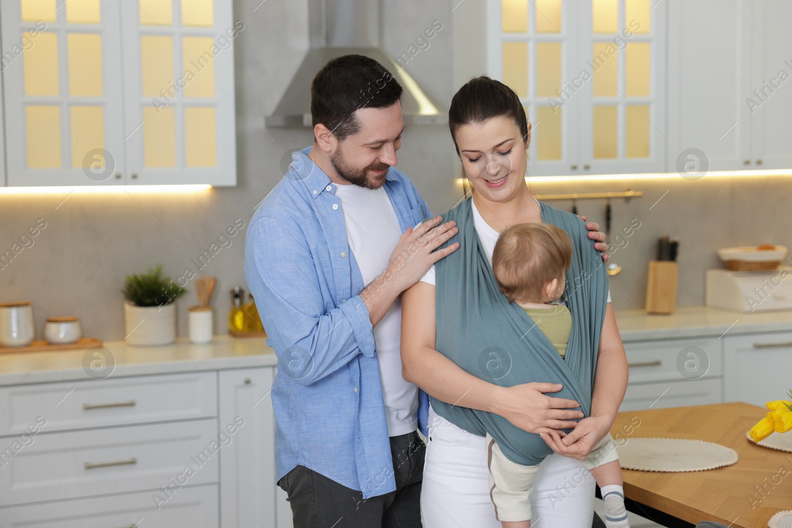 Photo of Portrait of happy family indoors, space for text. Mother holding her child in sling (baby carrier) at home