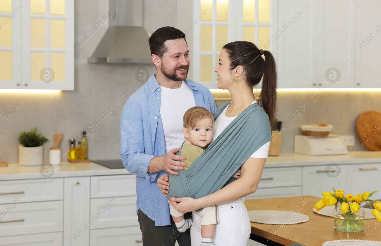 Photo of Portrait of happy family indoors, space for text. Mother holding her child in sling (baby carrier) at home