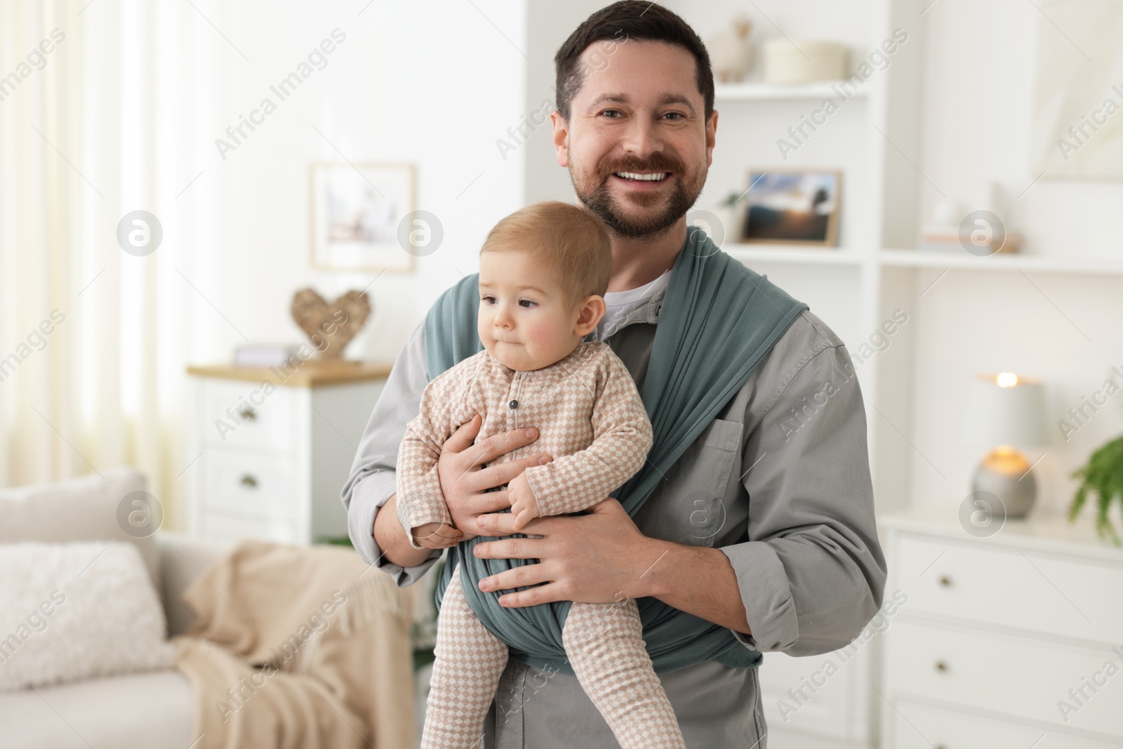 Photo of Father holding his child in sling (baby carrier) at home