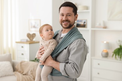 Photo of Father holding his child in sling (baby carrier) at home