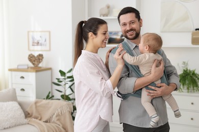 Photo of Portrait of happy family indoors, space for text. Father holding his child in sling (baby carrier) at home