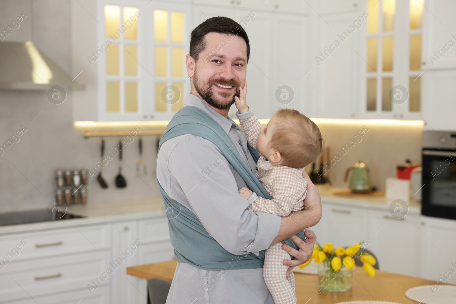 Photo of Father holding his child in sling (baby carrier) at home