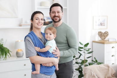 Photo of Portrait of happy family indoors. Mother holding her child in sling (baby carrier) at home