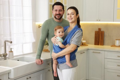 Photo of Portrait of happy family indoors. Mother holding her child in sling (baby carrier) at home