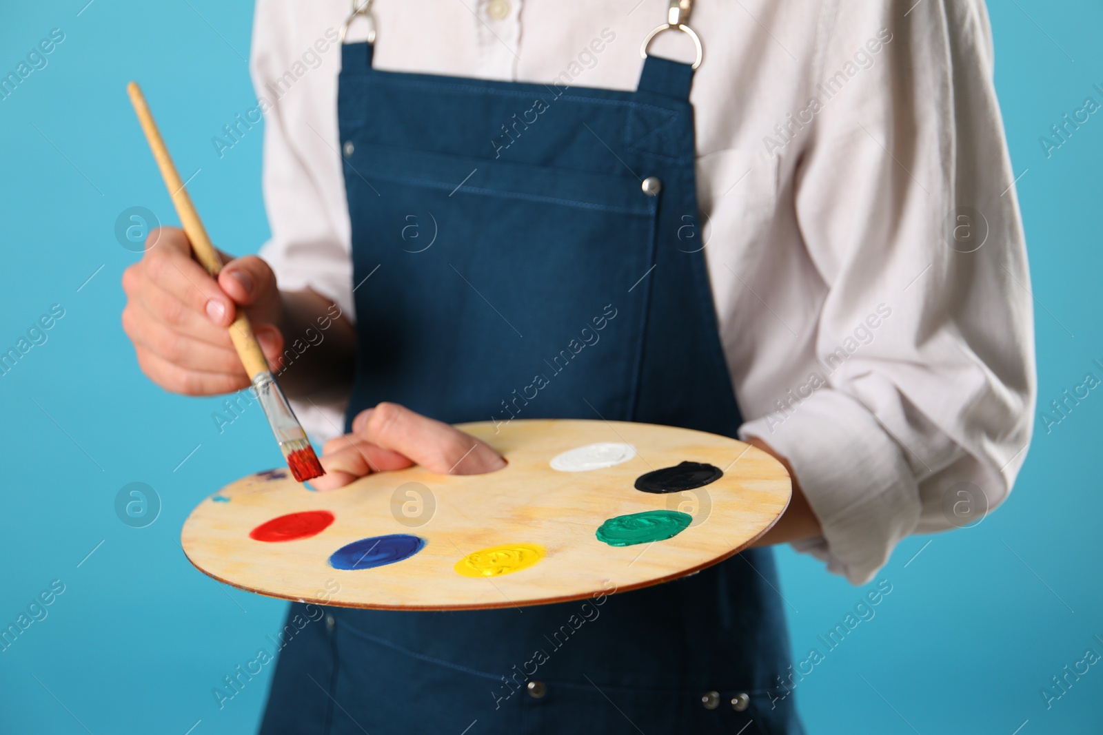 Photo of Man with wooden palette and paintbrush on light blue background, closeup