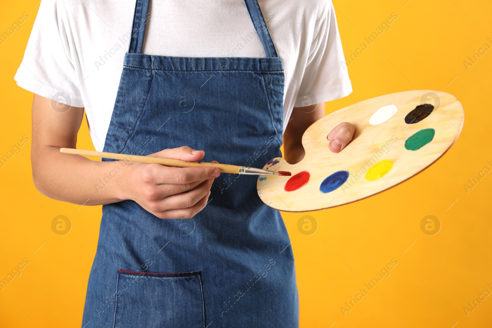 Photo of Man with palette and paintbrush on orange background, closeup