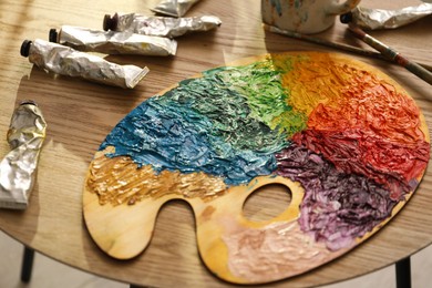 Photo of Wooden palette with bright paints, brush and tubes on table, closeup