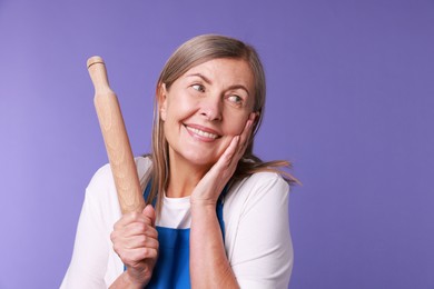 Photo of Happy woman with rolling pin on violet background. Space for text