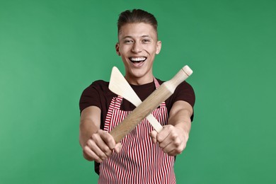 Photo of Happy man with rolling pin and turner on green background