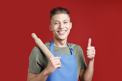 Photo of Happy man with rolling pin showing thumbs up on red background